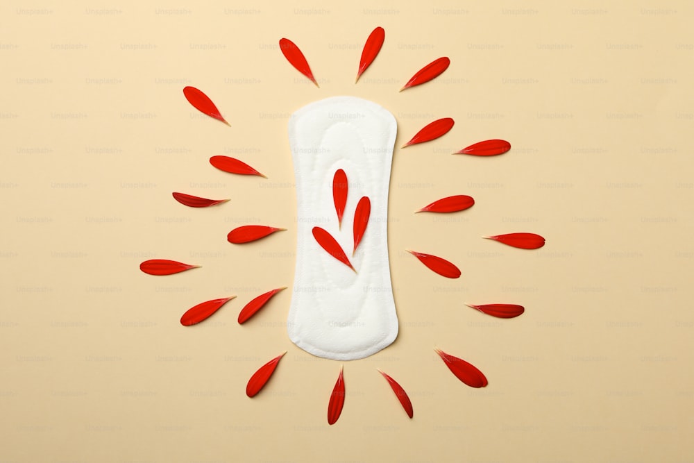 Sanitary pad with gerbera petals on beige background, top view