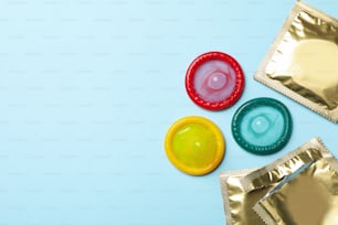 Multicolored condoms on blue background, space for text