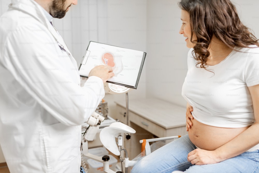 Medico con donna incinta durante un consulto medico in studio ginecologico, mostrando alcuni schemi medici per la comprensione. Concetto di assistenza medica e salute durante la gravidanza