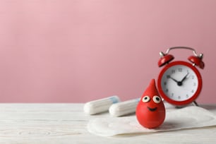 Sanitary pads with feather, decorative blood drop and alarm clock on wooden table, copy space