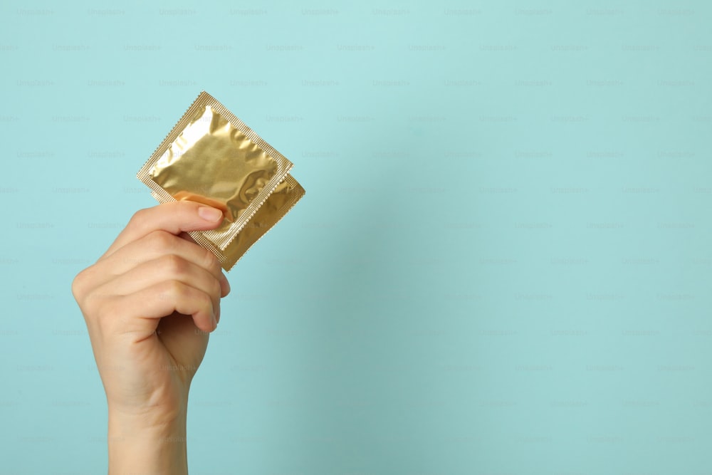 Female hand hold condoms on blue background, space for text
