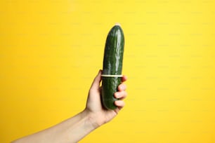 Woman hold cucumber with condom on yellow background, space for text