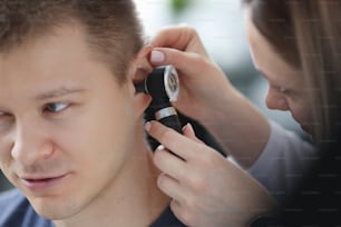 Otorhinolaryngologist examining ear of sick man with otoscope closeup. Diagnosis and treatment of ear diseases concept