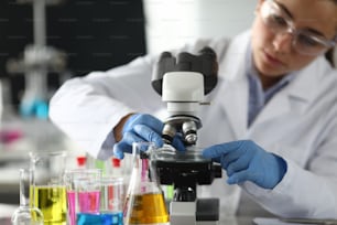 Close-up of researcher in protective glasses and gloves. Lab assistant making analysing sample of experiment in microscope. Chemical experiments concept