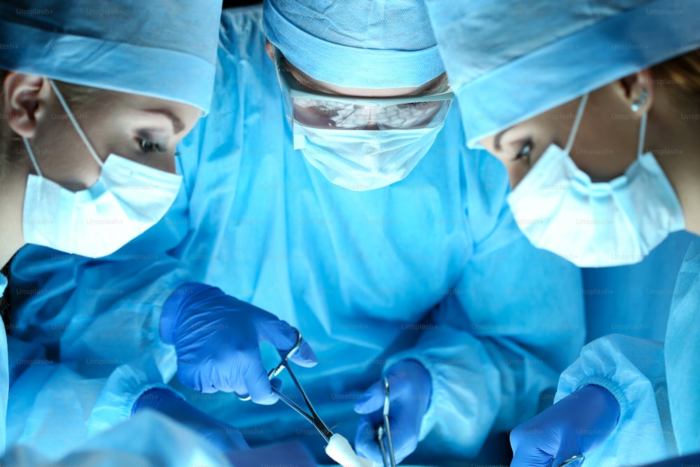 수술실에서 수술 중인 외과 의사 3명. 보호 마스크를 착용한 소생의료팀이 환자를 구하고 있습니다. 수술 및 응급 개념