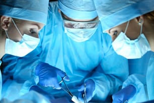 Three surgeons at work operating in surgical theatre. Resuscitation medicine team wearing protective masks saving patient. Surgery and emergency concept