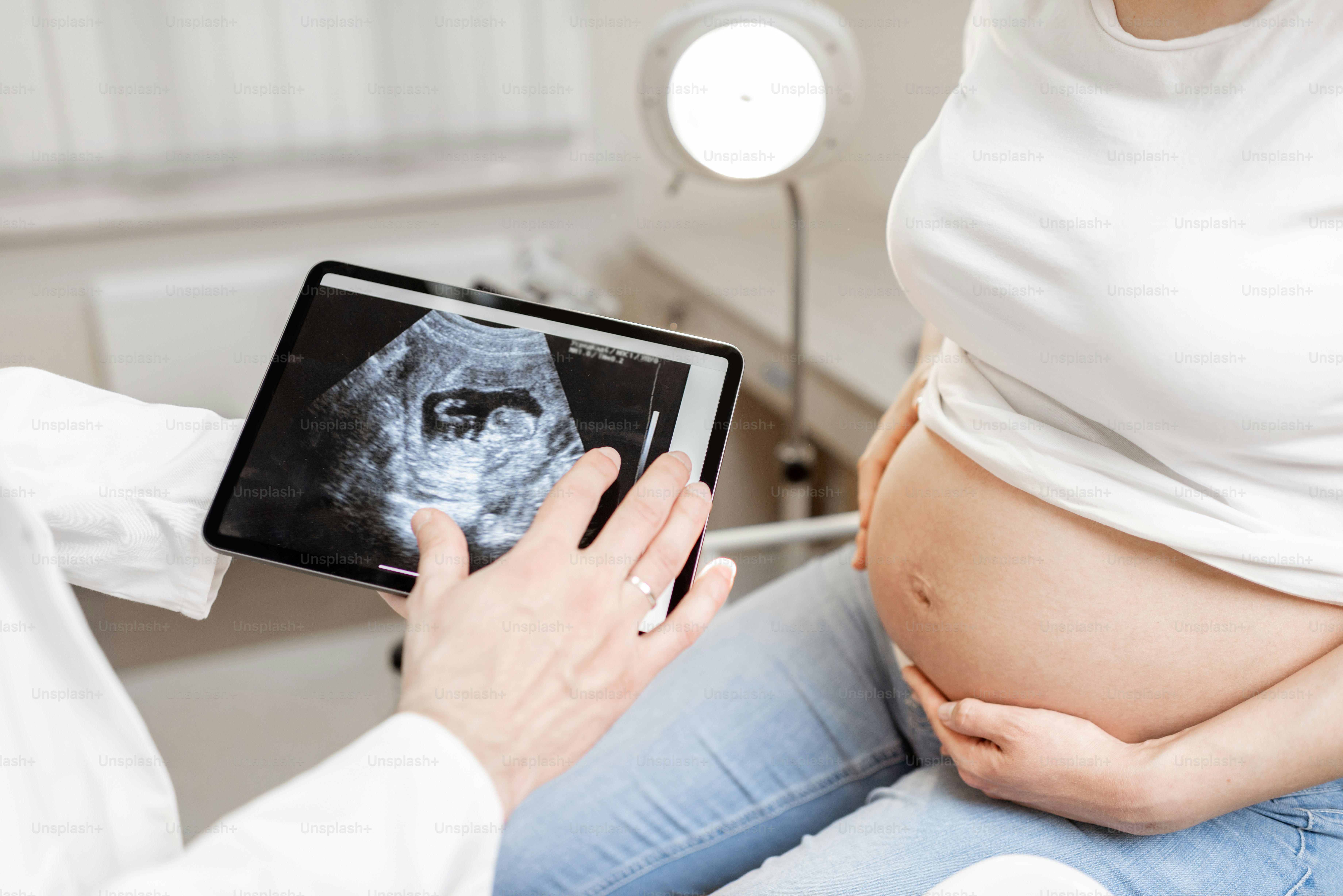 doctor with an ultrasound scan of unborn child on a digital tablet during an examination with a pregnant woman in the office, cropped view without faces