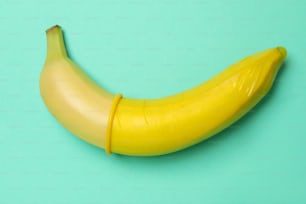 Banane avec préservatif jaune sur fond menthe