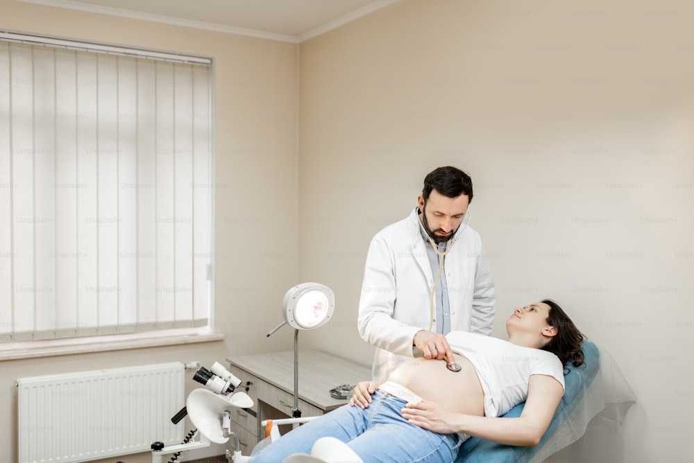 Médico que escucha el vientre de una mujer embarazada con un estetoscopio durante un examen médico. Concepto de atención médica y salud durante el embarazo