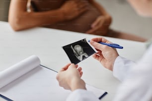 Close-up of doctor examining the embryo ultrasound image sitting at the table and talking to pregnant woman during her visit