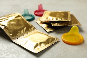 Multicolored condoms on white textured background, close up