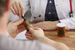 Close-up of doctor give bottle with extract oil of cannabis for health treatment. Man on appointment in clinic. Alternative medicine, healthcare concept