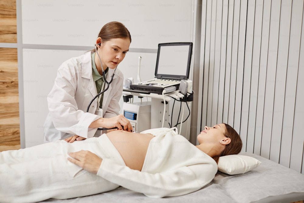 Portrait of female doctor examining pregnant young woman in ultrasound room at medical clinic