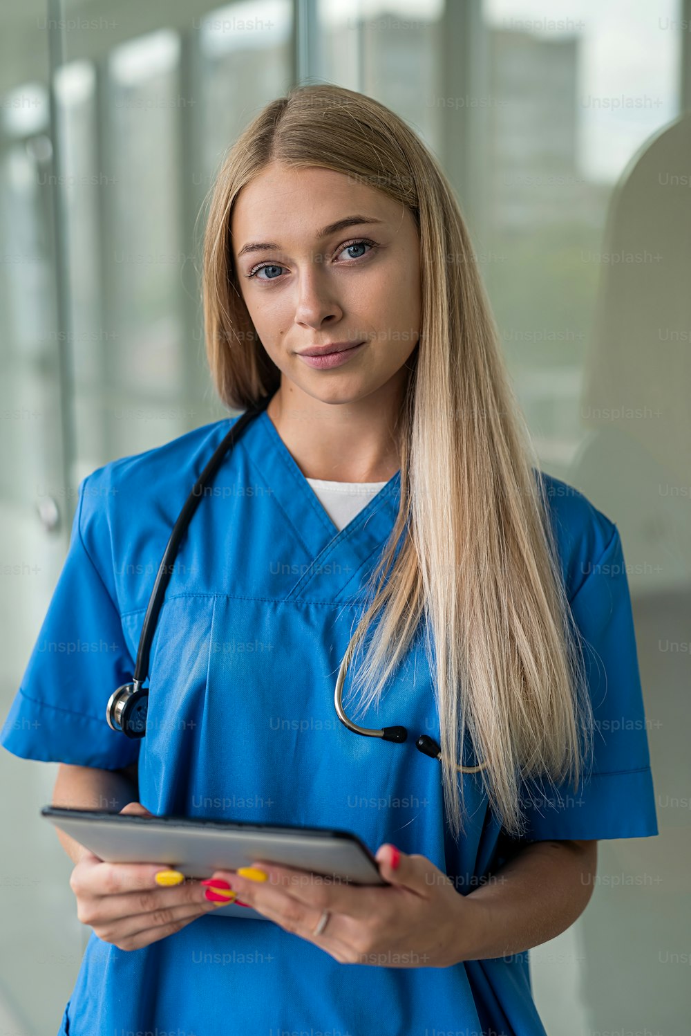Eine schöne junge Krankenschwester mit einem Stethoskop und einem Tablet steht im Flur. Medizin-Konzept
