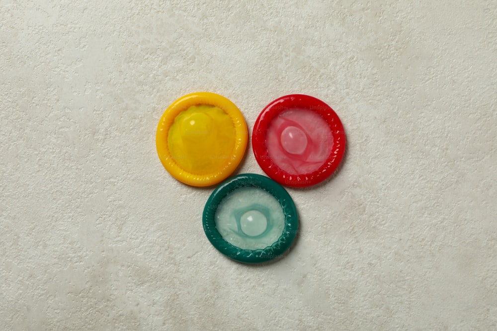 Multicolored condoms on white textured background, top view