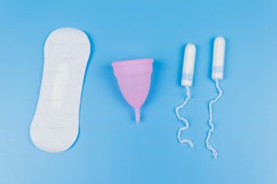 Absorvente, absorventes e coletor menstrual em fundo azul. Vista superior. Conceito de dias críticos, menstruação, higiene feminina