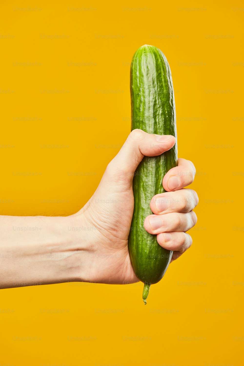 Cliché vibrant de la main tenant le concombre sur fond jaune concept de sexe sans risque
