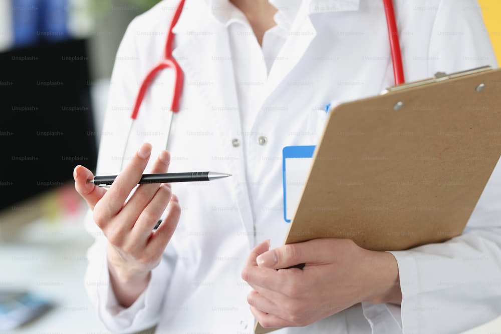 Doctor sosteniendo un portapapeles con documentos y bolígrafo en sus manos en primer plano. Concepto de gestión de registros médicos