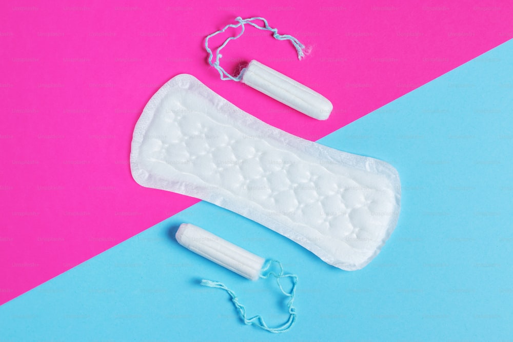 Toallas sanitarias y tampones para mujeres: las toallas sanitarias se encuentran junto a un tampón sobre un fondo aislado sobre un fondo rosa y azul. Concepto de higiene de la mujer y período menstrual