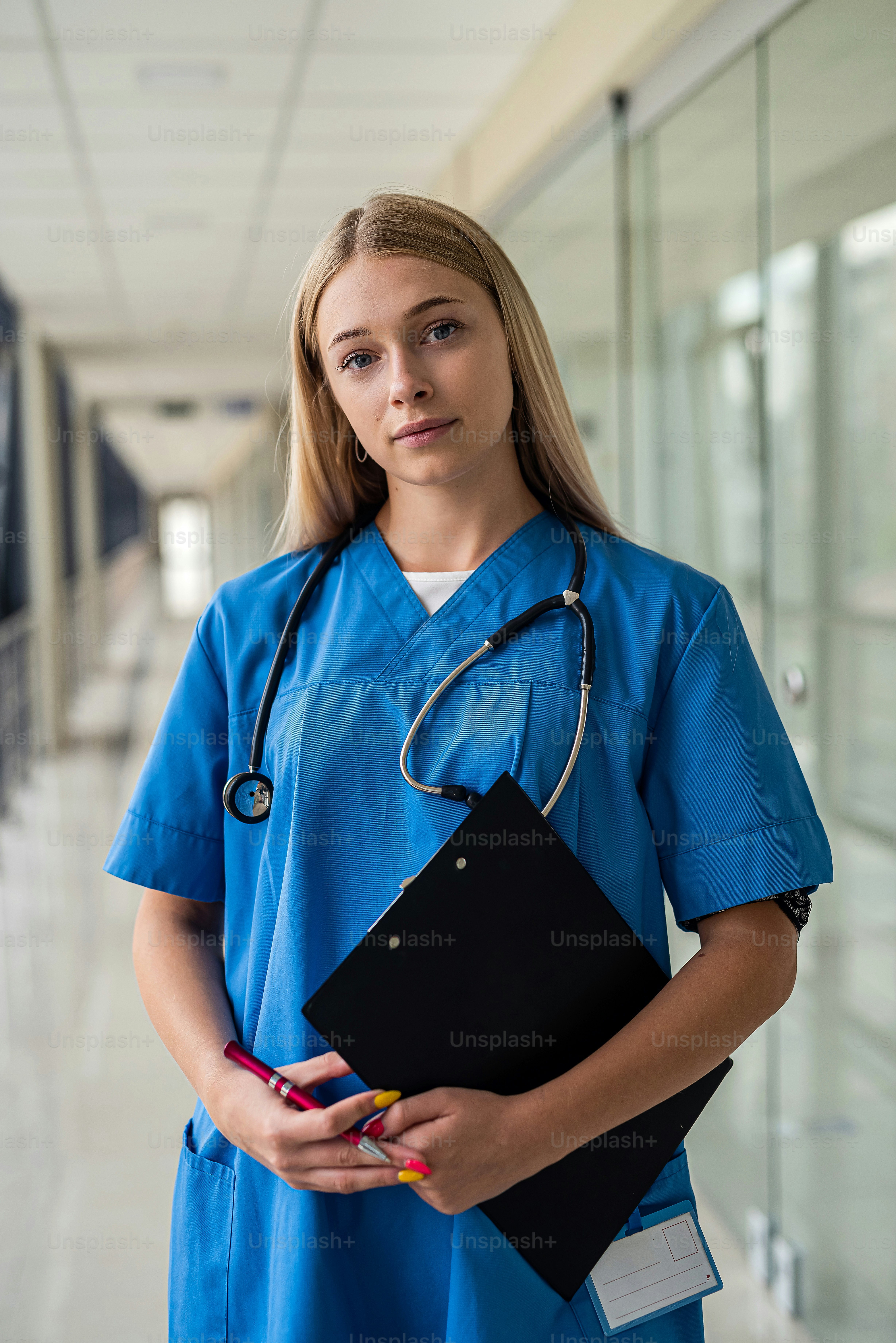 young beautiful nurse with a stethoscope around her neck and a tablet in her hands stands in the corridor of the hospital. Medicine concept