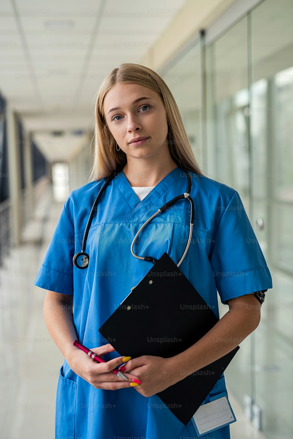 young beautiful nurse with a stethoscope around her neck and a tablet in her hands stands in the corridor of the hospital. Medicine concept