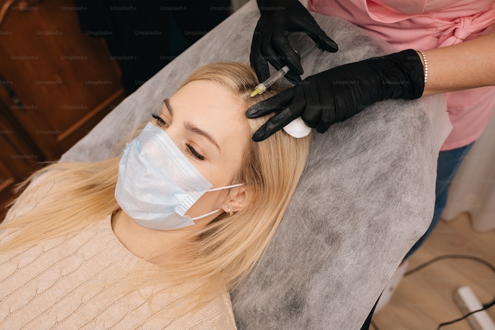 Beautician gloves gives injection into the head of blonde woman. Mesotherapy, hair loss therapy. Hair restoration concept.