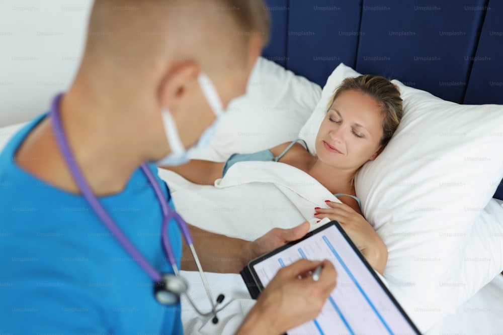Doctor makes notes in patient card and examines patient in bed. Medical care and health insurance concept
