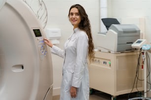 Medical doctor does computer tomography fot patient. Young girl in white coat looks in camera and press button on CT