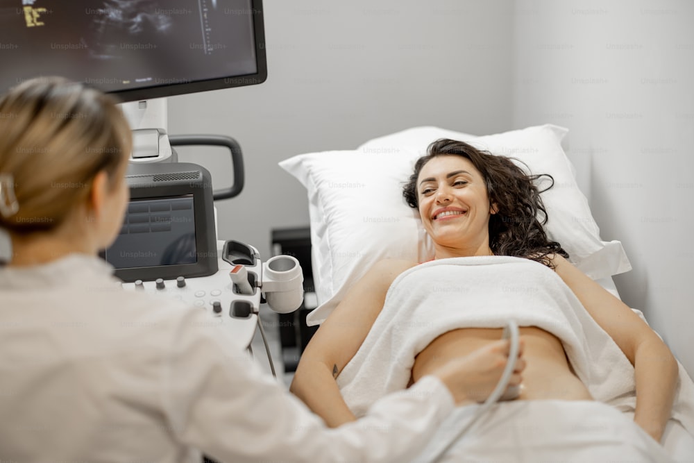 Glückliche erwachsene Frau bei einer Ultraschalluntersuchung der Bauchhöhle in einer modernen Arztpraxis. Konzept der Frauengesundheit und Untersuchung während der Schwangerschaft