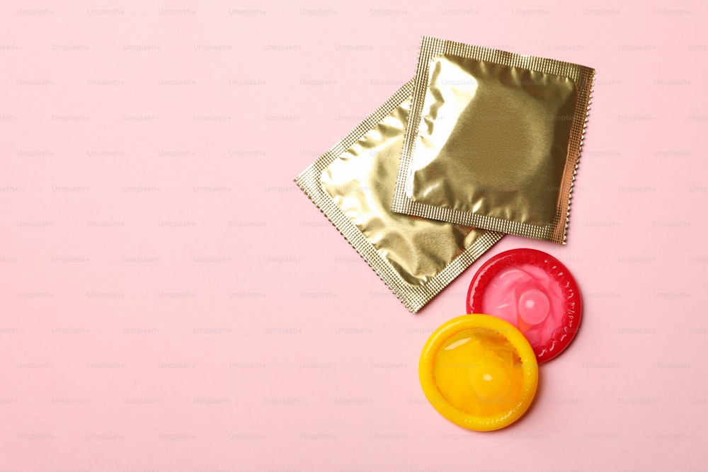 Preservativos amarillos y rojos sobre fondo rosa