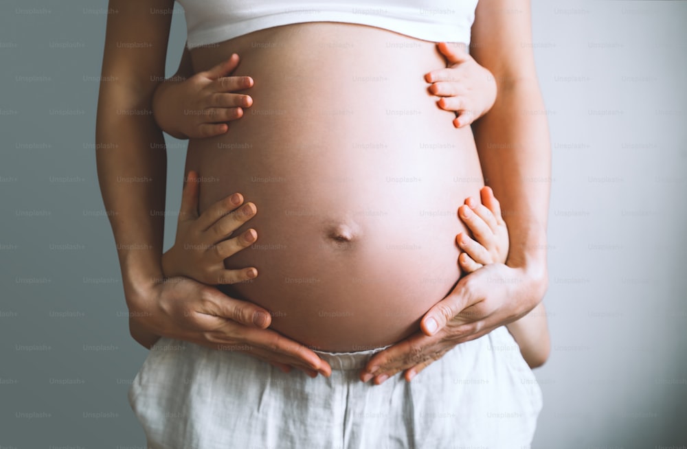 Concetto di famiglia, gravidanza, maternità, nuova vita. Primo piano bella pancia di donna incinta con le sue mani e le mani dei bambini che abbracciano la mamma. Mamma incinta e bambini in attesa del parto.