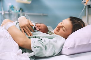 お母さんと新生児。産院での出産。出産後、生まれたばかりの赤ちゃんを抱きしめる若いお母さん。出産する女性。分娩後の赤ちゃんの人生の最初の瞬間。