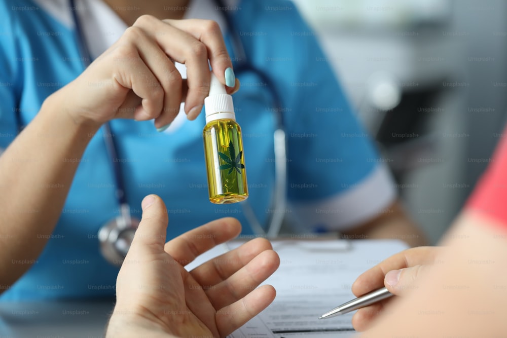 Focus on hand of professional physician giving to patient bottle of cannabinoid oil. Doctor speaking about appointment. Healthcare and medical marijuana concept