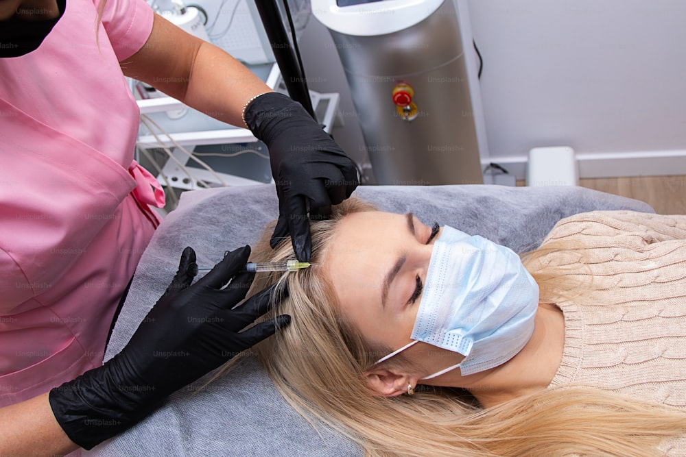 Woman getting injection into scalp, mesotherapy, hair loss therapy. Doctors wearing gloves in salon making medical manipulations to patient. Close-up photo