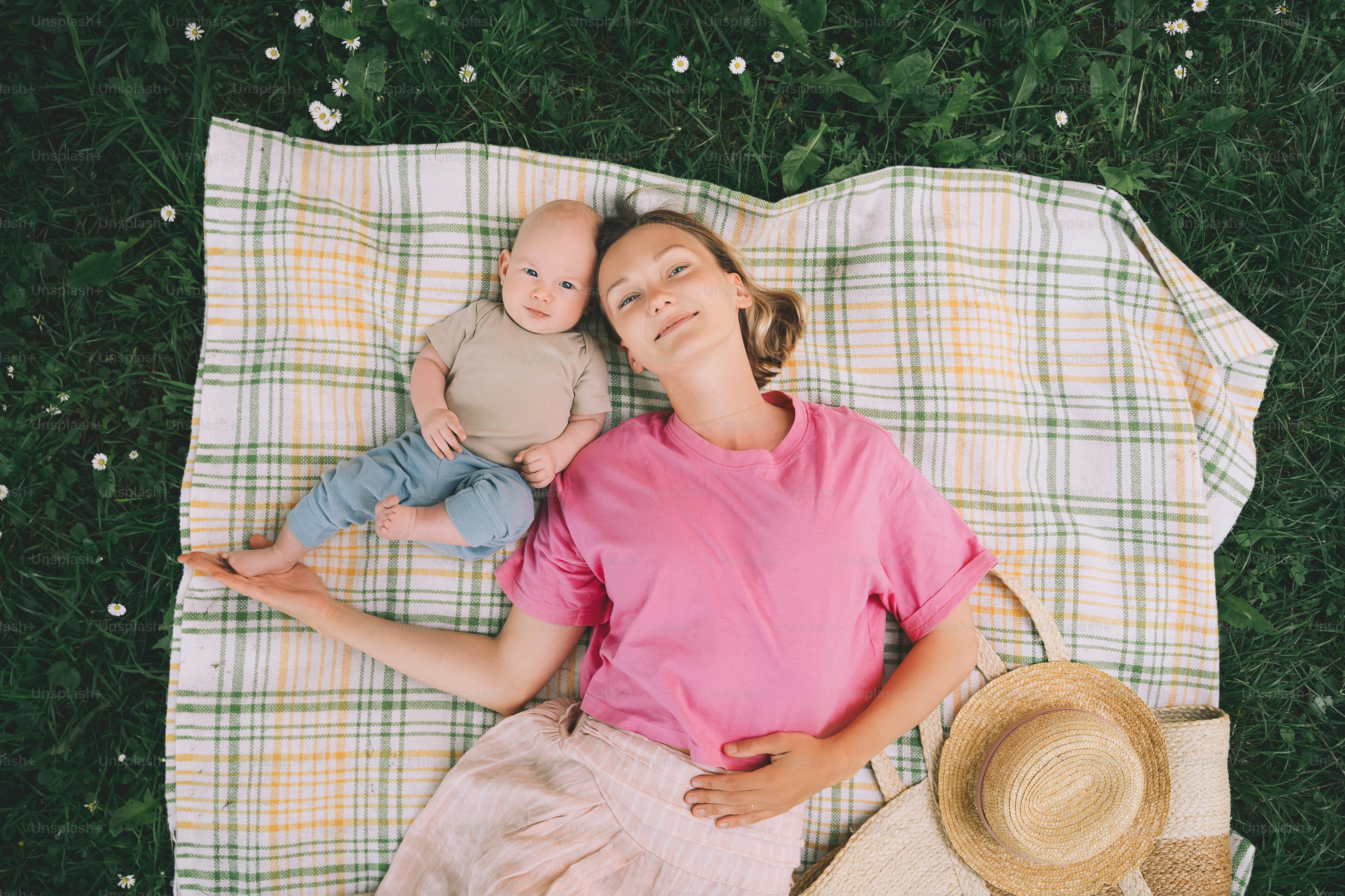 Maman souriante et bébé allongé sur une couverture sur l’herbe verte en été. Détente en famille et pique-en plein air. Belle maman avec son bébé sur la nature. Concept de maternité, de bonheur humain, de vie écologique.