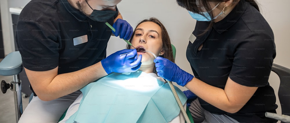 Un dentista di sesso maschile opera una giovane donna sorridente in una clinica odontoiatrica e un'assistente lo aiuta. concetto di igiene orale. denti sani lavarsi i denti