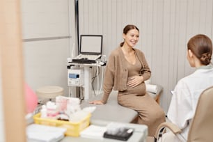 Portrait of pregnant young woman smiling happily while listening to doctor in ultrasound exam room