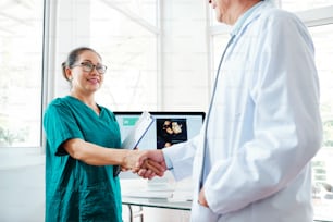 Smiling mature Vietnamese medical nurse shaking hand of doctor in office