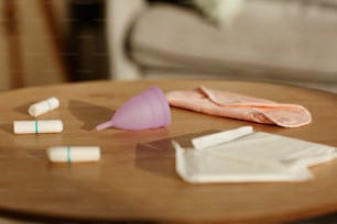 Imagen de fondo mínima de productos de higiene femenina variados en una mesa de madera con enfoque en la copa menstrual rosa, espacio de copia