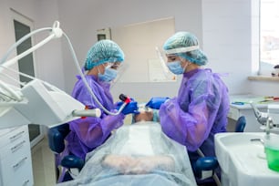 Dos hermosas ayudantes con ropa especial, máscaras, gorros, guantes, ayudan a llevar la operación al dentista. El concepto de cirugía dental