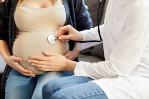 아기 심장 박동 소리를 듣는 알아볼 수 없는 산부인과 의사의 클로즈업, 임신한 배에 미시경을 놓는 것, 복사 공간