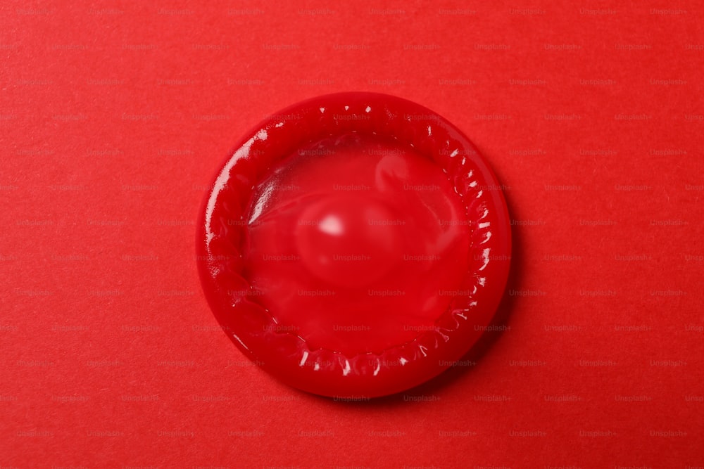 Single red condom on red background, top view