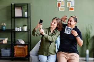 Portrait of young gay couple expecting baby and showing ultrasound image to family via video chat, same sex family lifestyle