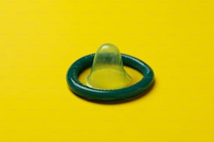 Einzelnes mintfarbenes Kondom auf gelbem Hintergrund, Nahaufnahme