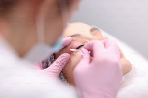 Beautician wiping cream on clients eyelid with cotton swab closeup. Permanent makeup concept