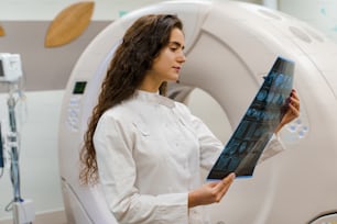 The young women doctor in medical gown looks at x-ray picture of patient brain after computer tomography. CT diagnostic in medical clinic