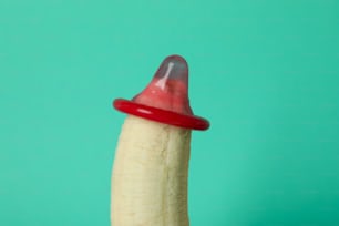 Banana con preservativo rosso su sfondo menta