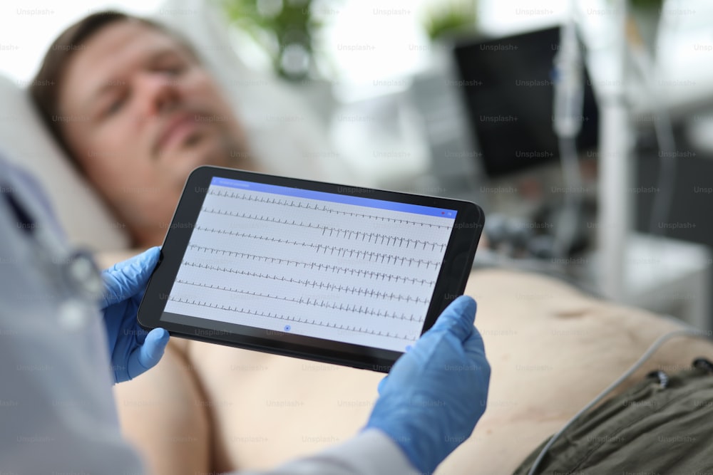 Focus on hands of female doctor examining condition of patient illness heart and touching screen of modern tablet with cardiogram. Medicine and healthcare concept