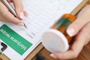 Close-up view of female doctor filling marijuana recipe for patient. Medical professional holding in hand jar with cannabis. Folk therapy and health concept