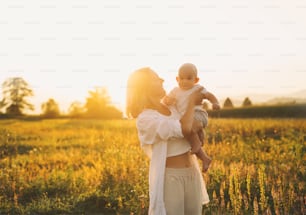 Loving mother and baby at sunset. Beautiful woman and small child in nature background. Concept of natural motherhood. Happy healthy family at summer outdoors. Positive human emotions and feelings.
